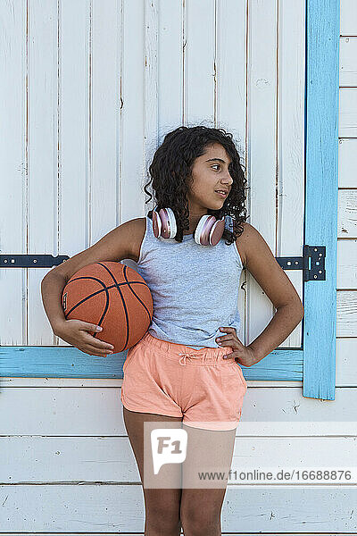 Porträt eines Mädchens mit lockigem Haar mit einem Basketball und Kopfhörern