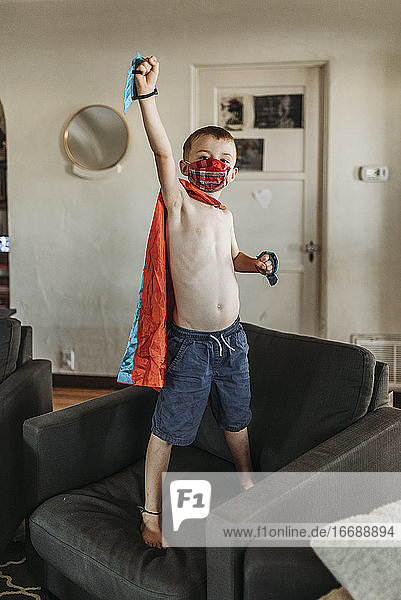 Junge als Superheld gekleidet steht auf Couch mit Maske auf