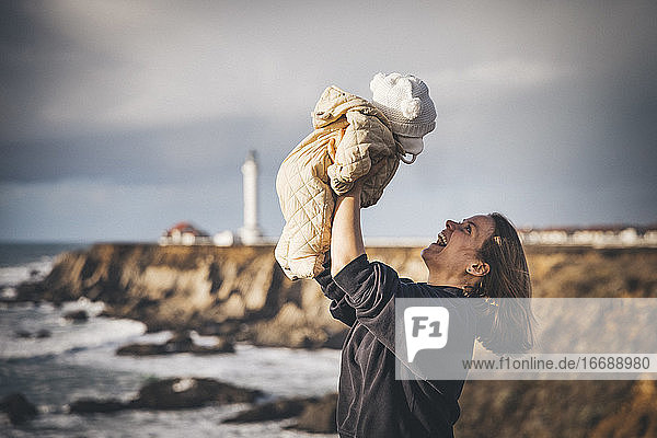 Eine Frau hält ein Baby in der Nähe eines Leuchtturms an der Pazifikküste