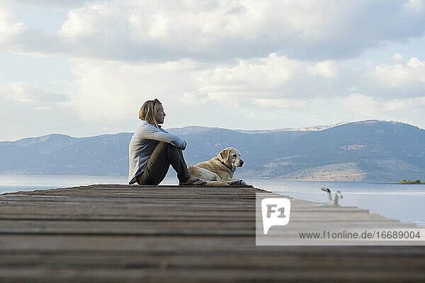 Eine Frau und ihr Hund genießen den Abend auf dem Steg am Hebgensee.