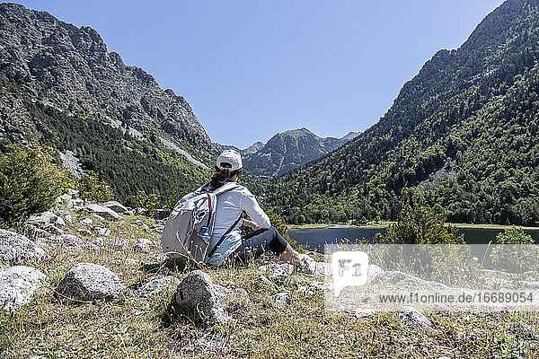 Female backpacker tourist in Spain looking at landscape while sitting on the rock in front of a lake.