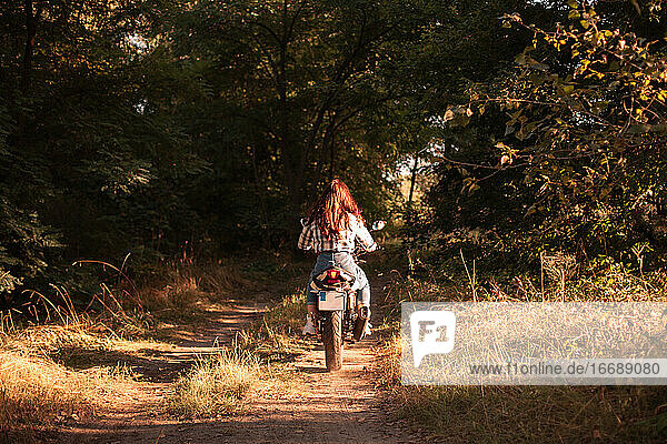 Back view of woman riding motorcycle on dirt road in forest