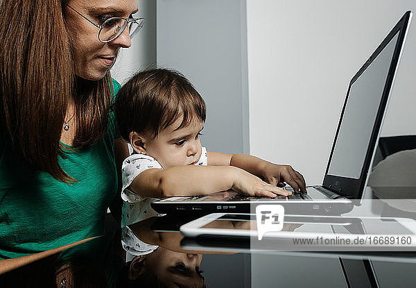 Beschäftigte Frau mit kleinem Kind arbeitet am Laptop