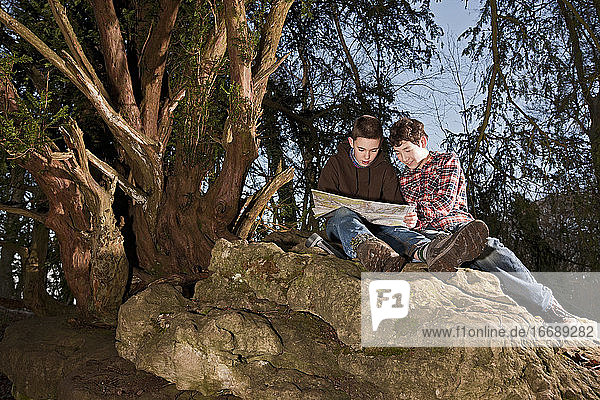 two boys reading map on top of rock
