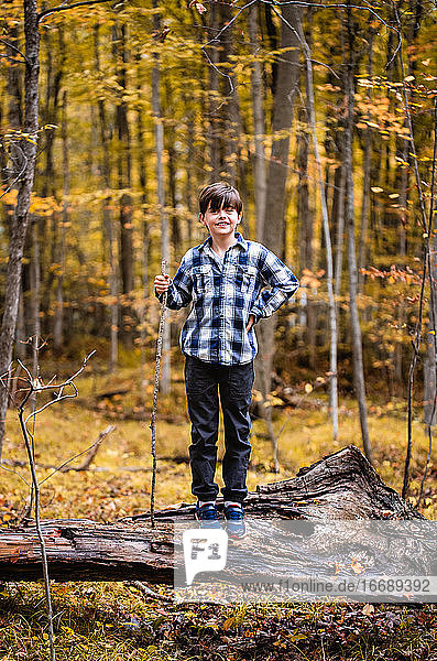 Young boy standing on a fallen tree in the woods on an autumn day.