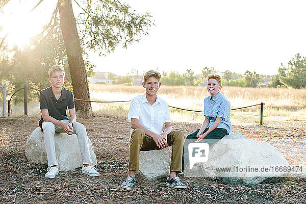 Portrait Outside Of Three Boys Sitting On Large Rocks