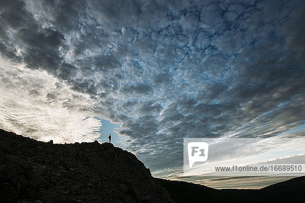 Person auf Berg in Silhouette mit dramatischen Wolken in Maine