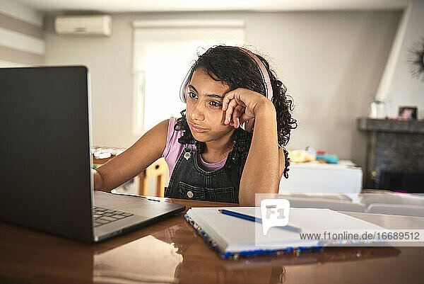 Ein gelangweiltes Mädchen macht zu Hause ihre Hausaufgaben mit ihrem Laptop