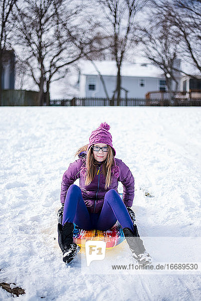 Pre-Teenie auf Schlitten im Schnee sitzend im Winter