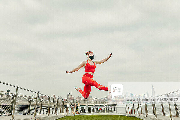Junge Sportlerin springt in der Luft und trägt eine Gesichtsmaske am Ufer