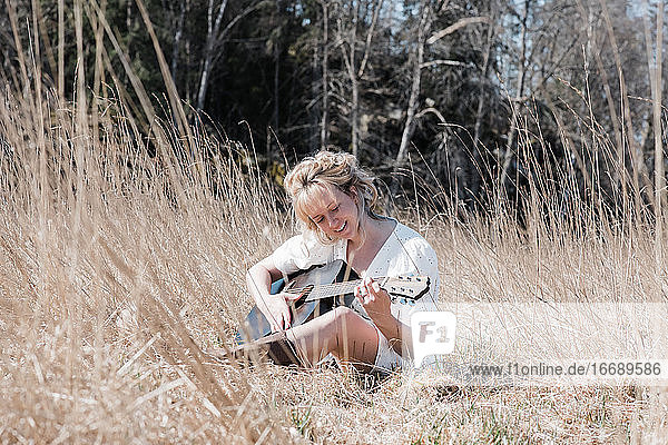 Frau saß auf einem Feld und spielte fröhlich Gitarre im Sommer