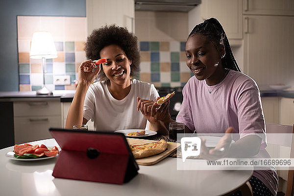 Frauen  die online chatten  während sie sich zu Hause eine Pizza teilen