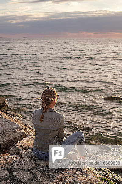 Rückenansicht einer jungen Frau  die auf das Meer blickt