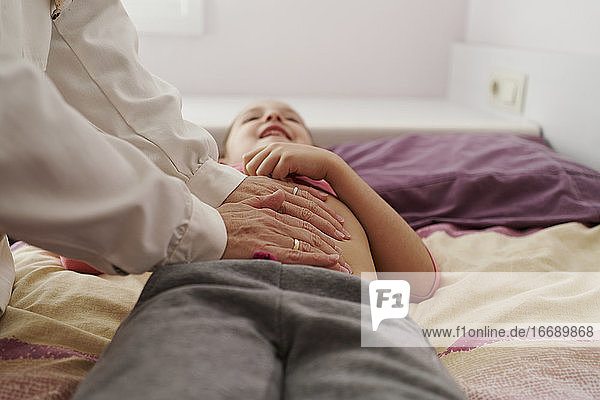 Ärztin  die den Unterleib eines kleinen Mädchens in ihrem Zimmer untersucht. Hausarzt-Konzept