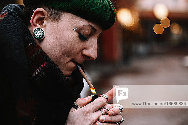 Porträt einer nicht-binären Hipster-Frau  die sich in der Stadt eine Zigarette anzündet