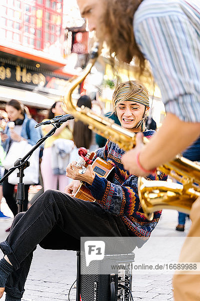 Selektiver Fokus auf das Gesicht eines singenden Mannes  der neben einem Saxophonisten auf der Straße Gitarre spielt