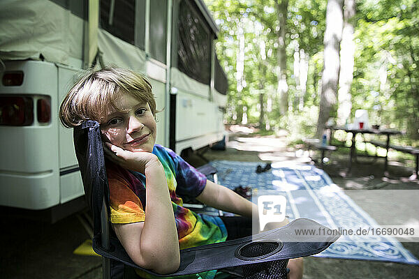 Junger Junge in Tie Dye Shirt sitzt in Camping Stuhl vor Pop Up