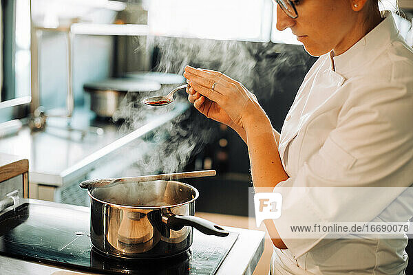 Female chef seasoning hot food while standing at stove