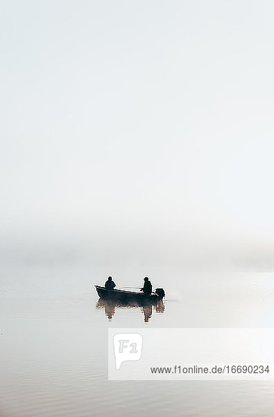 Mann und Kind beim Angeln in einem Boot bei dichtem Nebel auf einem See.