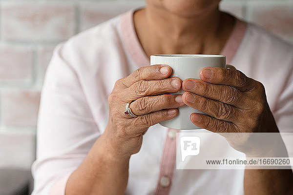 Alte Frau hält eine Tasse heißen Kaffee zu Hause trinken