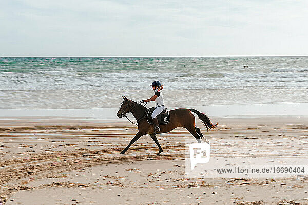 Frau reitet auf andalusischem Pferd am Strand in Spanien