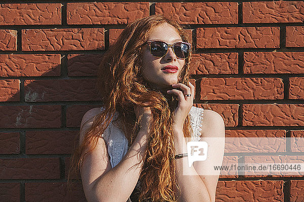 Porträt einer jungen rothaarigen Frau  die sich an eine Backsteinmauer lehnt