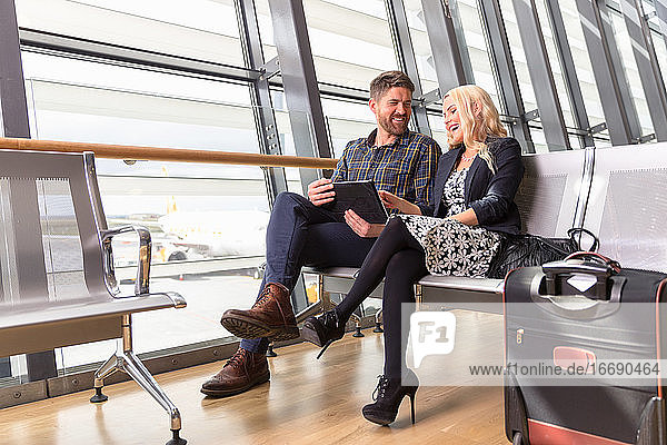 Glückliches Paar benutzt Tablet im Flughafen