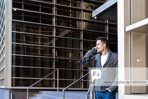 Mann benutzt Smartphone im Freien  neben einem Bürogebäude stehend