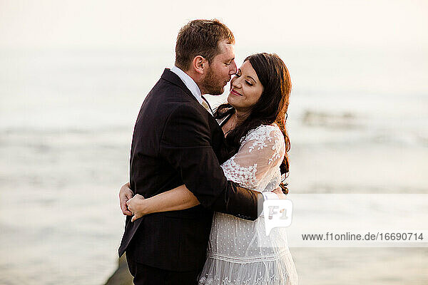 Newlyweds Standing on Rock at Beach in San Diego During Sunset