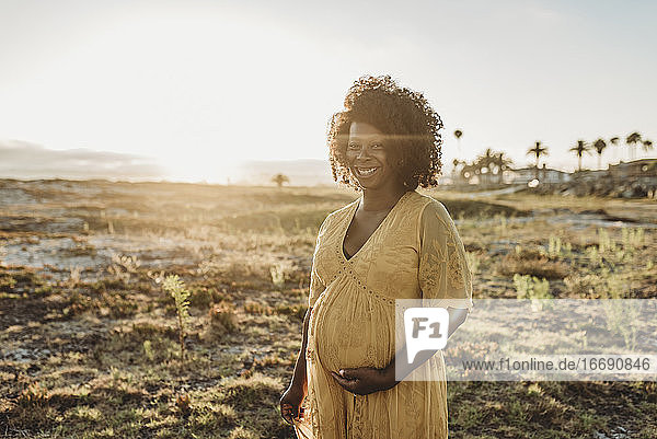 Porträt einer schwangeren Mutter im dritten Trimester am Strand bei Sonnenuntergang