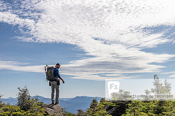 Mann mit Rucksack steht auf einem Felsen auf dem Gipfel eines Berges.