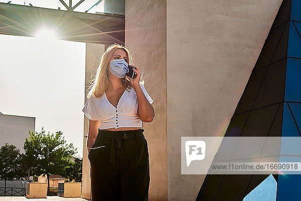 Young woman talks on the phone while wearing a mask
