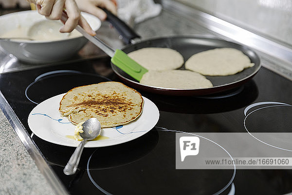 Anonyme Person  die Pfannkuchen mit einem Spatel in einer Pfanne wendet  in der Teig gebacken wird