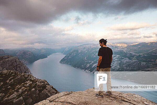 Mann steht und schaut auf den Rand einer Klippe am Preikestolen  Norwegen  hinunter