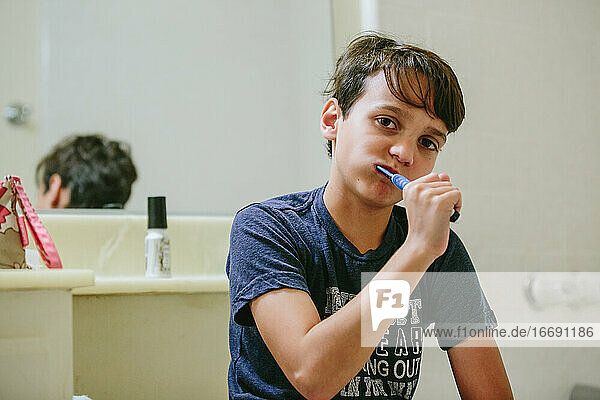 Boy brushes his teeth in the bathroom while looking at the camera