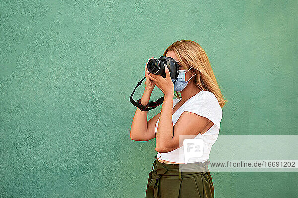 Young woman with a mask and a camera on a green background
