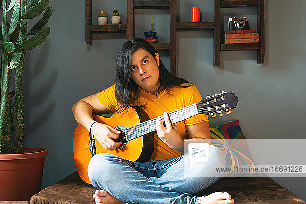 Mann mit langen Haaren spielt Akustikgitarre zu Hause während der Quarantäne