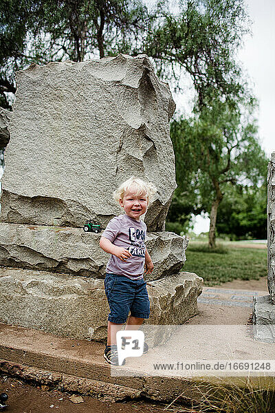 Zweijähriges Kind lächelt und steht neben einem Felsen