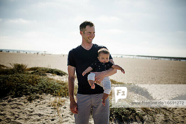Father Casually Standing on Beach Holding Infant Son