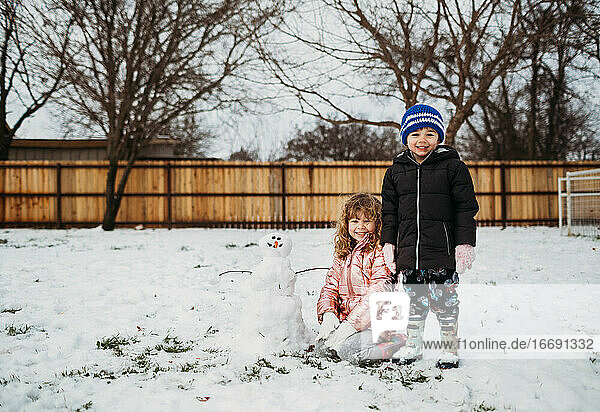 Junge Geschwister bauen im Winter draußen einen Schneemann
