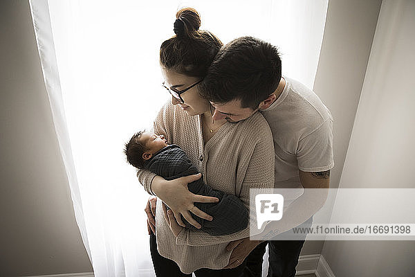 Gen Z Parents Snuggle by Window and Admire Their Newborn Baby
