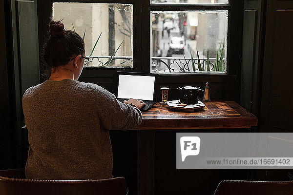 Ein junger Student arbeitet an einem Tisch in der Nähe eines Kneipenfensters