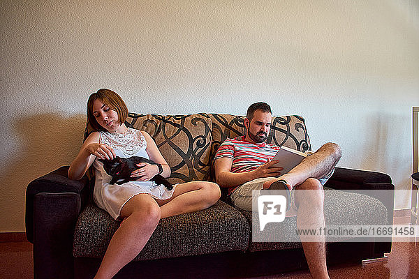 Ein Ehepaar sitzt zu Hause auf der Couch. Er liest und sie streichelt eine Katze