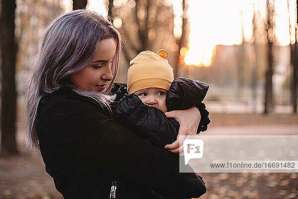 Junge Mutter hält süßes Baby Sohn im Park im Herbst bei Sonnenuntergang