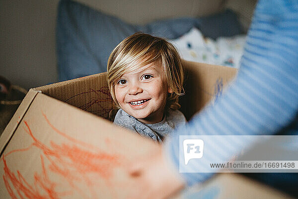 Junges männliches Kind  das lächelnd in die Kamera schaut und in einer Schachtel spielt