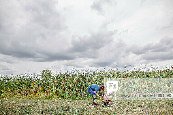 Two boys play together by tall cattails on a cloudy day