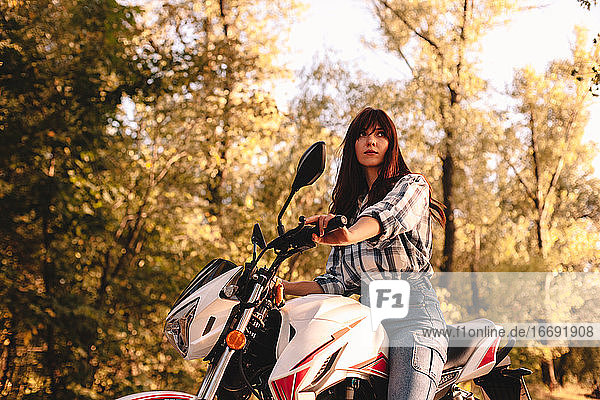 Selbstbewusste junge Frau fährt Motorrad inmitten von Bäumen im Wald
