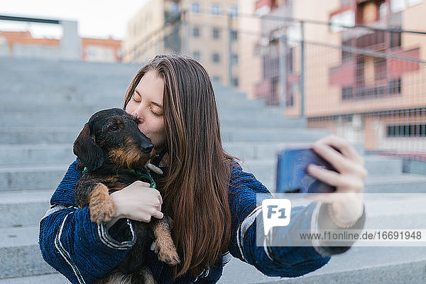Schöne junge erwachsene Frau  die ein Selfie-Foto macht und ihren Hund küsst