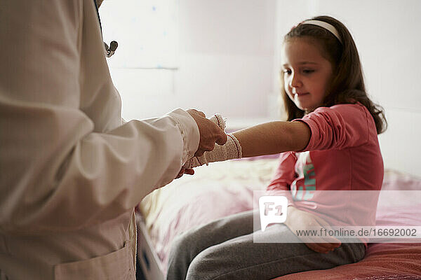 Female doctor bandaging the arm of a little girl in her room. Home doctor concept