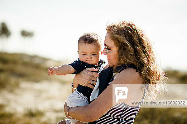 Grandmother Holding & Snuggling Grandson While Standing on Beach